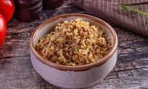 Bol rempli de quinoa, un aliment aux multiples quinoa bienfaits, avec des tomates et des épices en arrière-plan.