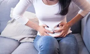 Femme assise sur un canapé, se tenant le ventre, possiblement à cause d'une inflammation de l'utérus.
