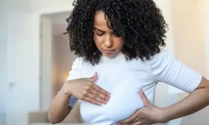 Femme aux cheveux bouclés examinant sa poitrine, inquiète des symptômes de mastite infectieuse.