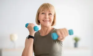 Femme souriante faisant du sport avec haltères bleus, un exemple de sport ménopause pour rester en forme.