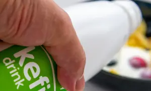 Main d'une personne versant du kéfir dans un bol de fruits. Découvrez les bienfaits du kéfir pour votre santé.