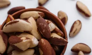 Un bol rempli de noix du Brésil, dont les bienfaits pour la santé sont nombreux. Quelques noix sont dispersées autour.