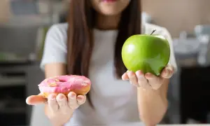 Choix entre une pomme verte et un donut rose. Le donut est un exemple d'aliments mauvais pour la flore intestinale, contrairement à la pomme.