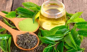 Cuillère de thé vert en vrac, poudre de matcha et verre de thé infusé, entourés de feuilles fraîches. Découvrez les thé vert bienfaits.