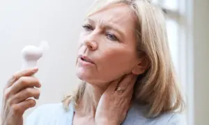 Femme blonde utilisant un petit ventilateur pour soulager les bouffées de chaleur de la préménopause. Elle a l'air inconfortable.