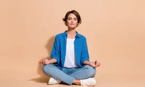 Femme en tenue décontractée, assise en tailleur, les yeux fermés, pratiquant la méditation.