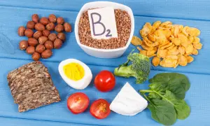 Assortiment d'aliments riches en vitamine B2 : sarrasin, noisettes, œuf, pain complet, tomates, brocolis, épinards, fromage et flocons de maïs.