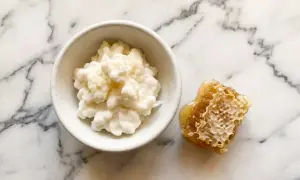 Un bol de kéfir crémeux à côté d'un morceau de nid d'abeille dégoulinant de miel. Attention, le kéfir peut présenter un danger s'il n'est pas préparé correctement.