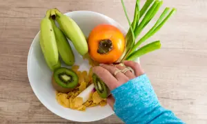 Bol de fruits avec banane, kaki, kiwi et céréales. Une main prépare une collation saine pour aider à prévenir une infection urinaire.
