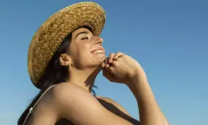 Jeune femme souriante sous un chapeau de paille, profitant du soleil pour sa vitamine D. Ciel bleu clair.