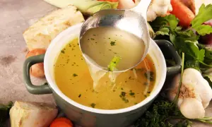 Un bouillon réconfortant, idéal pour soulager les maux d'estomac et la diarrhée. Des légumes frais entourent le bol.
