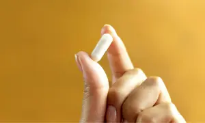 Main tenue pour votre bien-être : 1g de vitamine C par jour, une capsule blanche tenue entre le pouce et l'index.