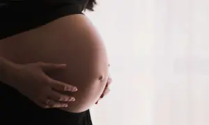 Gros plan sur le ventre arrondi d'une femme enceinte, ses mains le caressant. Un signe que la perte du bouchon muqueux approche.