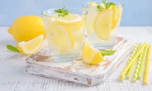 Deux verres de limonade pétillante avec des tranches de citron et des feuilles de menthe. Un citron entier et une tranche sont à côté. Parfait pour soulager les gaz intestinaux.