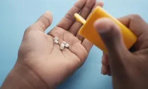 Main tenant une pilule dans sa paume, une main verse d'autres pilules d'un flacon jaune. Le maltitol peut présenter un danger.