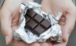 Mains tenant une tablette de chocolat noir déballée, rappelant ses bienfaits pour la santé et le plaisir.