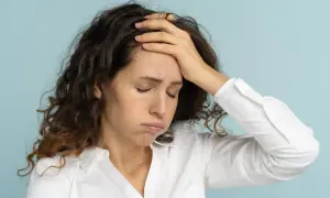 Femme aux cheveux bruns, le visage marqué par la fatigue mentale, une main sur le front, les yeux fermés.
