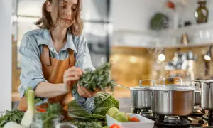 Une femme prépare des herbes fraîches dans une cuisine. La cuisson à haute température peut entraîner la destruction de certaines vitamines.