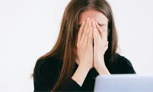 Une jeune femme, le visage caché par ses mains, exprime une **énorme fatigue** devant son ordinateur.