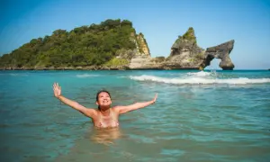 Une femme rayonnante profite des bienfaits de l'eau de mer dans un décor paradisiaque, bras ouverts vers le ciel bleu.