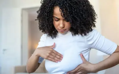 Femme aux cheveux bouclés examinant sa poitrine, inquiète des symptômes de mastite infectieuse.