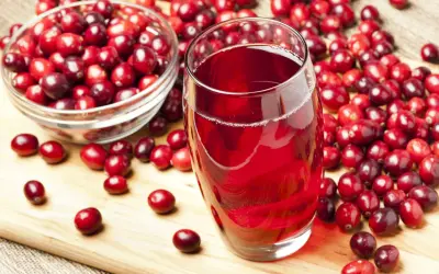 Un verre de jus de cranberry rouge vif, entouré de baies fraîches. Est-ce que le cranberry fait uriner ? Cette boisson est connue pour ses bienfaits.
