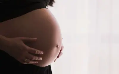Gros plan sur le ventre arrondi d'une femme enceinte, ses mains le caressant. Un signe que la perte du bouchon muqueux approche.
