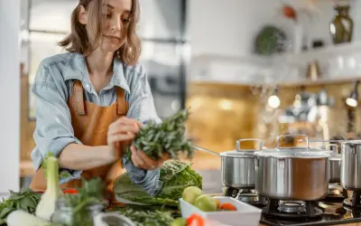 Une femme prépare des herbes fraîches dans une cuisine. La cuisson à haute température peut entraîner la destruction de certaines vitamines.