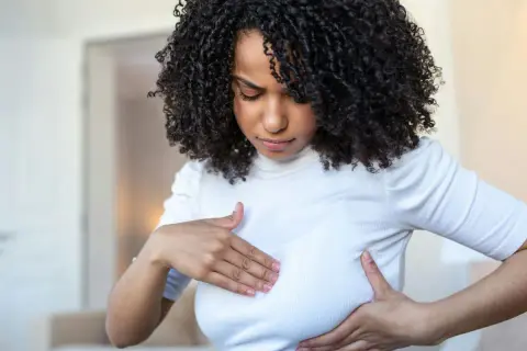 Femme aux cheveux bouclés examinant sa poitrine, inquiète des symptômes de mastite infectieuse.