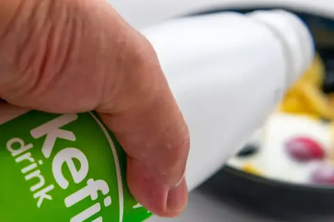 Main d'une personne versant du kéfir dans un bol de fruits. Découvrez les bienfaits du kéfir pour votre santé.