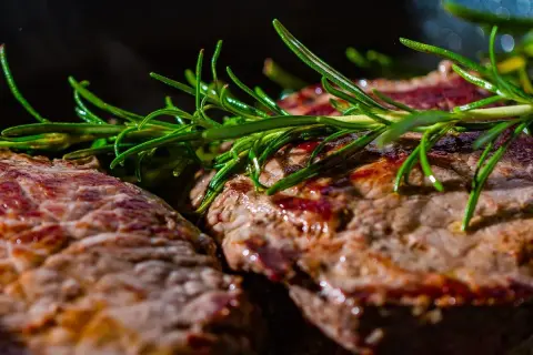 Deux steaks grillés, parsemés de romarin frais. Ces aliments riches en glutamine sont parfaits pour la récupération musculaire.