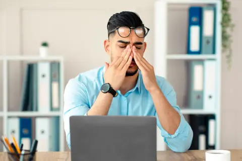 Homme fatigué au bureau, se frottant les yeux devant son ordinateur. Que faire contre la fatigue ?