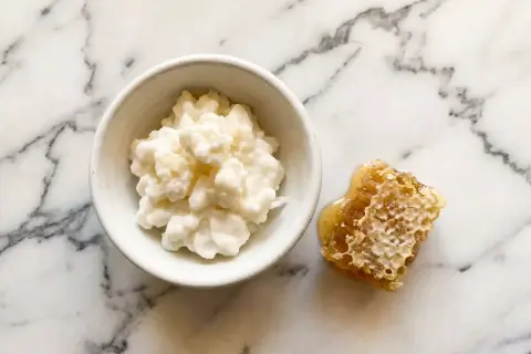 Un bol de kéfir crémeux à côté d'un morceau de nid d'abeille dégoulinant de miel. Attention, le kéfir peut présenter un danger s'il n'est pas préparé correctement.