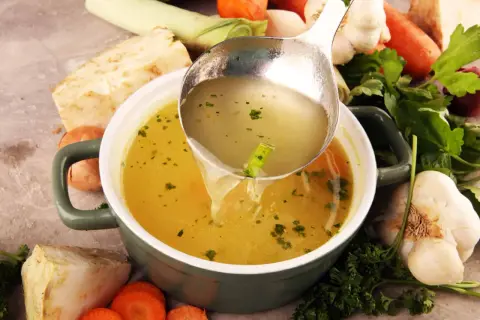Un bouillon réconfortant, idéal pour soulager les maux d'estomac et la diarrhée. Des légumes frais entourent le bol.
