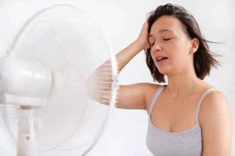 Une jeune femme étouffe sous la chaleur, sa main sur son front, cherchant un soulagement face au danger des bouffées de chaleur.