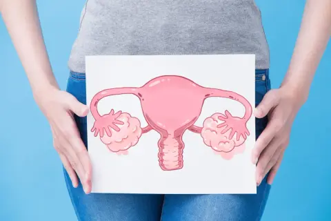Une femme tient une illustration d'organes reproducteurs féminins, symbolisant peut-être une mycose ou des douleurs aux ovaires.