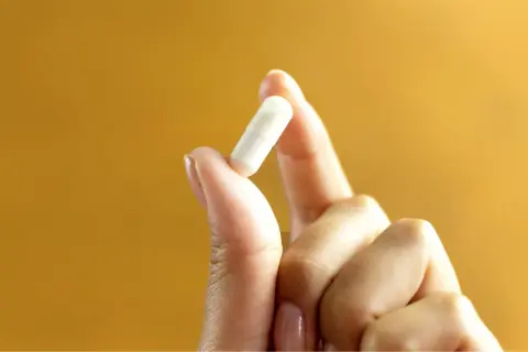 Main tenue pour votre bien-être : 1g de vitamine C par jour, une capsule blanche tenue entre le pouce et l'index.
