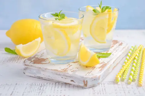 Deux verres de limonade pétillante avec des tranches de citron et des feuilles de menthe. Un citron entier et une tranche sont à côté. Parfait pour soulager les gaz intestinaux.