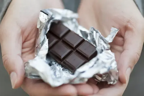 Mains tenant une tablette de chocolat noir déballée, rappelant ses bienfaits pour la santé et le plaisir.