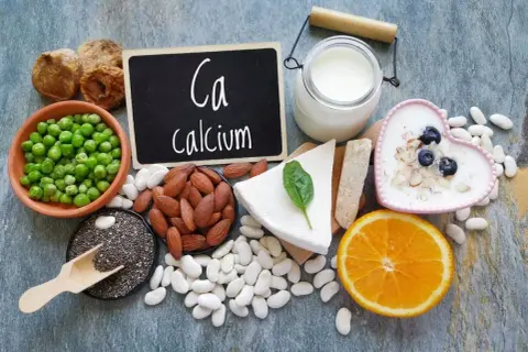 Assortiment d'aliments riches en calcium : lait, yaourt, fromage, amandes, haricots blancs, pois, figues séchées, graines de chia et orange.