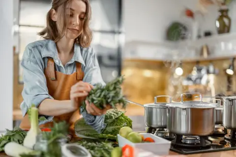 Une femme prépare des herbes fraîches dans une cuisine. La cuisson à haute température peut entraîner la destruction de certaines vitamines.