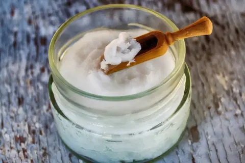 Un pot d'huile de coco avec une petite cuillère en bois. Attention, l'huile de coco danger pour la santé est un sujet de débat.