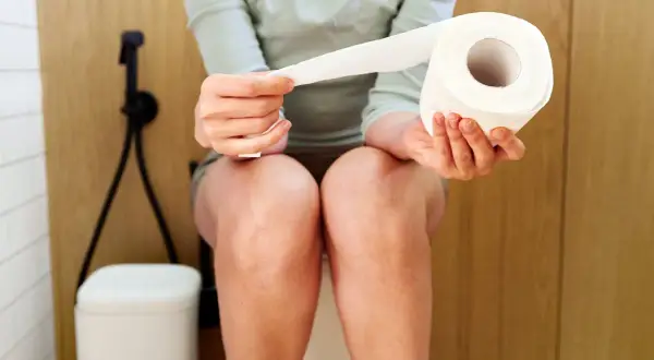Une personne assise sur des toilettes tient un rouleau de papier toilette. La question est : est ce que les probiotiques constipent ?