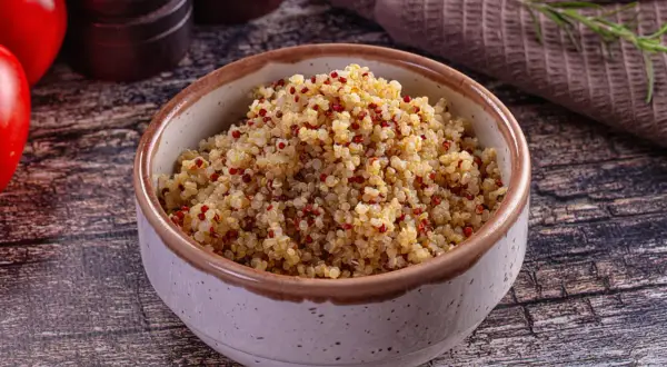 Bol rempli de quinoa, un aliment aux multiples quinoa bienfaits, avec des tomates et des épices en arrière-plan.