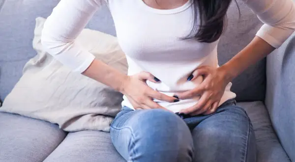 Femme assise sur un canapé, se tenant le ventre, possiblement à cause d'une inflammation de l'utérus.