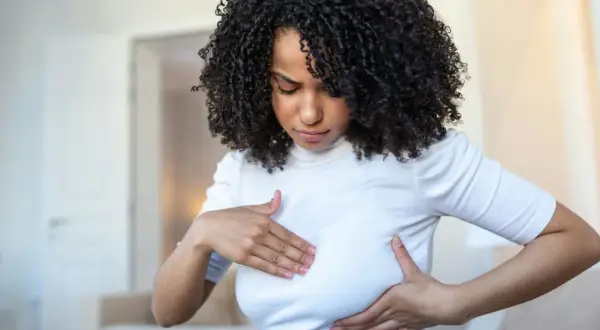 Femme aux cheveux bouclés examinant sa poitrine, inquiète des symptômes de mastite infectieuse.