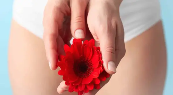 Mains délicates tenant une fleur rouge, symbolisant le soin et le désir de restaurer la flore vaginale.