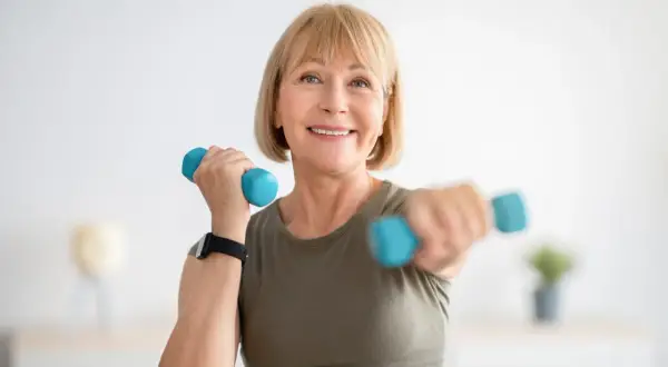 Femme souriante faisant du sport avec haltères bleus, un exemple de sport ménopause pour rester en forme.