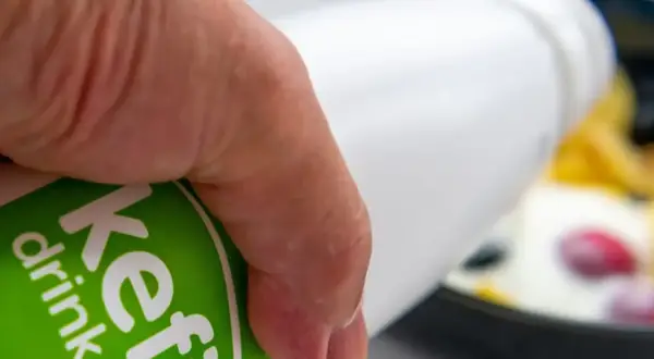 Main d'une personne versant du kéfir dans un bol de fruits. Découvrez les bienfaits du kéfir pour votre santé.