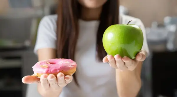 Choix entre une pomme verte et un donut rose. Le donut est un exemple d'aliments mauvais pour la flore intestinale, contrairement à la pomme.